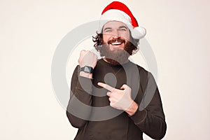 Pleased young bearded man is pointing at his smart wrist watch.