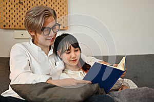 Pleased young couple reading book and spending leisure weekend time together at home