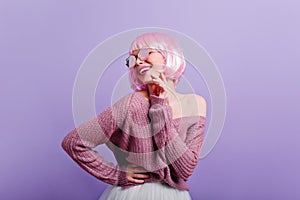 Pleased young girl in periwig and sunglasses having fun in studio. Photo of wonderful female model with pink hair