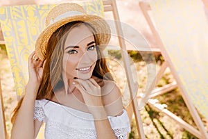 Pleased young woman with amazing green eyes relaxing in chaise-longue in garden spending summer with pleasure. Close-up