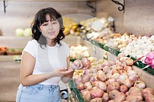 Pleased young woman purchaser choosing onion in grocery store
