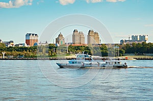 A pleasure boat moves down the river with the embankment of Heihe, China in the background. Beautiful blue sky with