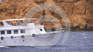 Pleasure Boat with Tourists is Sailing in the Storm Sea on background of Rocks. Egypt