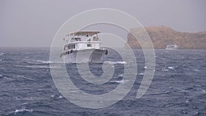 Pleasure Boat with Tourists is Sailing in the Storm Sea on background of Rocks. Egypt