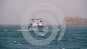 Pleasure Boat with Tourists is Sailing in the Storm Sea on background of Rocks. Egypt