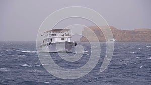 Pleasure Boat with Tourists is Sailing in the Storm Sea on background of Rocks. Egypt