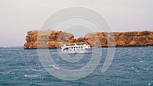 Pleasure boat with tourists is sailing in the storm sea on background of rocks. Egypt