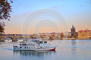 Pleasure boat on the Vltava River in Prague against the backdrop of Charles Bridge at sunset