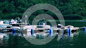 Pleasure boats and their reflections in the water at a marina near a steep mountain with forest trees in evening light