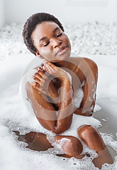 Pleasure and cleanliness. African american girl with closed eyes takes bath with foam