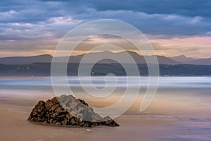 Plettenberg Bay beach at sunset, with hills in the distance and a rock in the foreground.