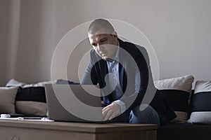 06.09.2022 - Pleven,Bulgaria - Young attractive man sitting on sofa at home working on laptop online, using internet, smiling,