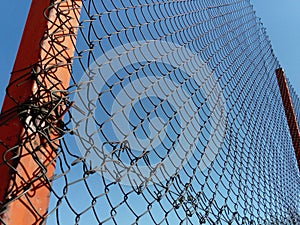 Plexus wire. Metal mesh netting attached to a pole. Part of the fence on the sports ground. In the background is a blue sky.