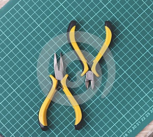a plier and a pincers on dark green grid mat