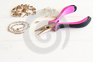 Pliers, chain, metal rings and pendants on wooden background. How to do yourself metal bracelet. Step