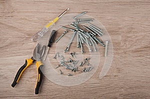 Pliers, screwdrivers and different size screws lay on table