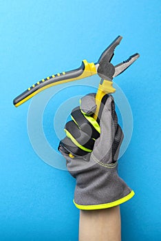 Pliers. Yellow and black pliers in the hand of an electrician on a blue monochrome background. Repair and installation tool.