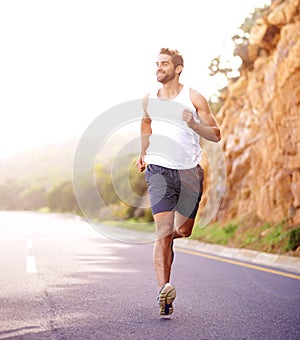 Plodding down the road of fitness. Full length shot of a handsome young man running on a road.