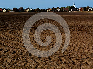 Ploughed  brown soil of rural farm land and village in the background