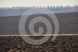Ploughed field in spring. Hills and forest on horizon. Clear sky
