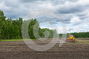 Ploughing tractor working on field, preparing soil for sowing with seedbed cultivator. Agricultural machinery, farming equipment