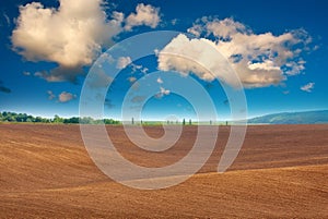 Plowed agricultural field soil on background of rural landscape and mystical sky with white clouds