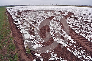 Plowed autumn field with first snow and tractor tracks