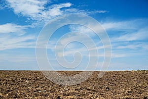 Plowed field and blue sky, soil and clouds of a bright sunny day - concept of agriculture