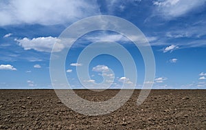 Plowed field, soil and clouds of a bright sunny day - concept of agriculture