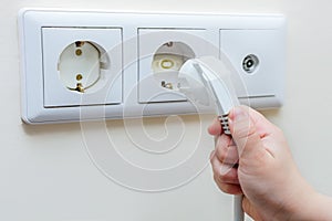 The plug from the electrical appliance is in the child`s hand, the child is trying to plug it into the socket, the socket is