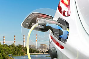 Plug of power cable electric supply during charging at ev car electric vehicle charging on electric power plant with smokestack