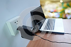 Plug in power outlet adapter cord charger on a white wall of the laptop computer on Wooden