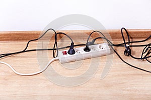 Plug strip with a red on off switch on the floor, white power extension cord plugs connected to it, tangled black wires, european