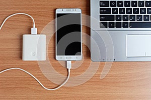 Plug in USB charger from powerbank input mobile phone or cell phone and laptop computer on wooden floor