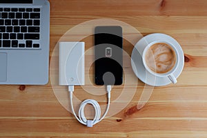 Plug in USB charger from powerbank input mobile phone or smartphone and laptop computer and coffee cup cappuccino on wooden floor,