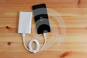 Plug in USB charger from powerbank input mobile phone or smartphone on wooden floor, Top view