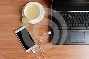 Plug in USB cord charger of the mobile phone with a laptop and freshly Lime juice in a white cup, on wooden floor