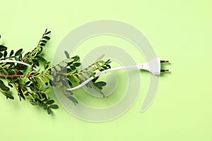 Plug wire with branch of green leaves on green background. Concept of saving energy, protecting the environment and conserving
