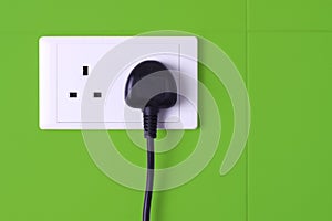 Plugged in socket against green tiles background