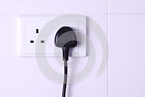 Plugged in socket against white tiles background
