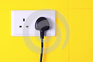 Plugged in socket against yellow tiles background