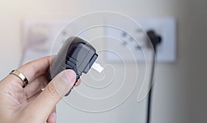 Plugging a black electrical plug with a woman's hand into a white plastic socket on a wall