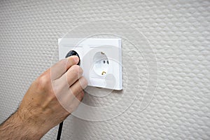 Plugging electrical, black plug in white electric socket on wall.