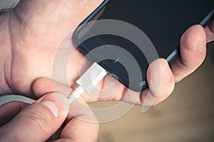 Plugging Out A White USB Cable Connected With A Black Mobile Phone, Holded By Male Hands