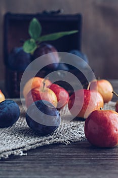 Plum and apples on a wooden table with a canvas cloth and a small chest.