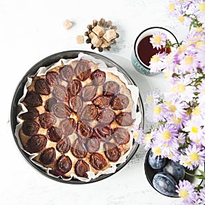 Plum cake with tea mug, fresh plums, brown sugar and flowe