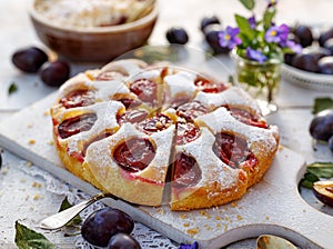 Plum cake, traditional homemade  cake with fruit, divided into portions, sprinkled with powdered sugar on a white board, close-up