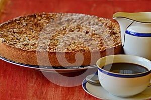 Plum crumble tart with cup of coffee and creamer on red background