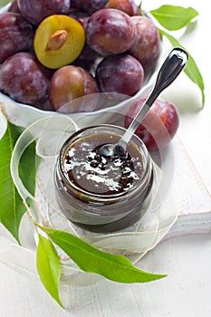 Plum jam in a glass jar and fresh fruits with leav