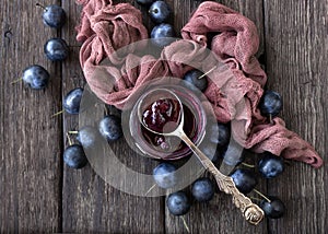 Plum jam in a glass jar with a spoon and ripe plums on a wooden table